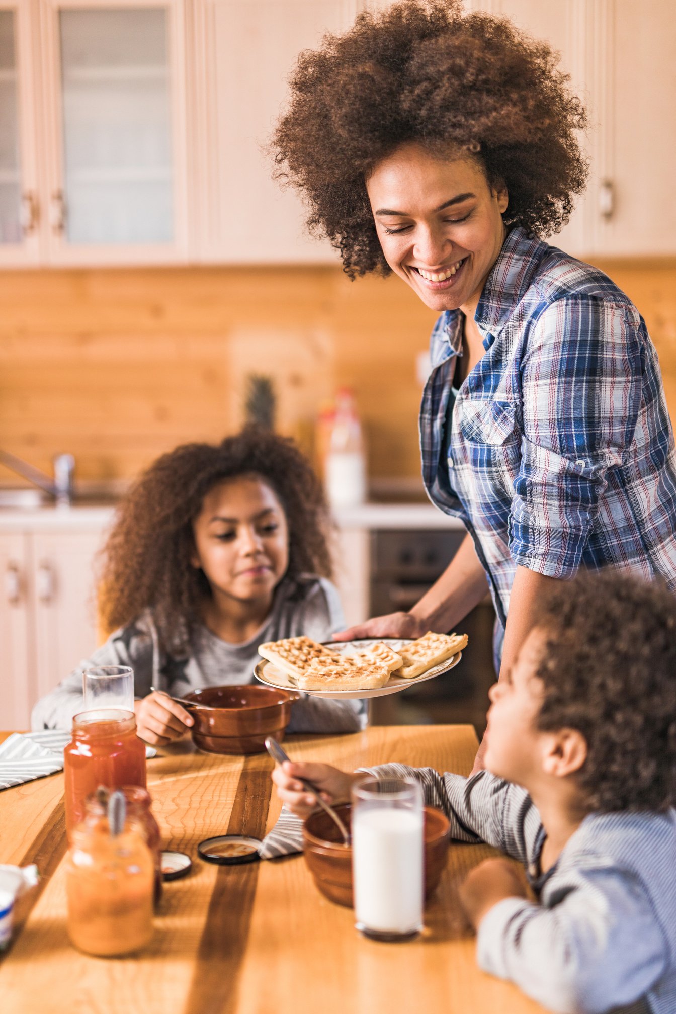 Happy black mother serving her kids Belgian waffles for breakfast.